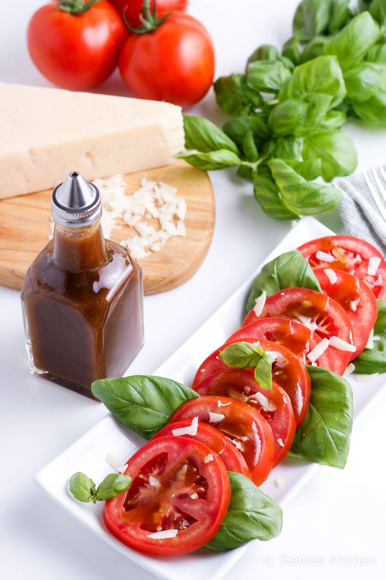 Balsamic vinegar dressing drizzled on a tomato and mozzarella salad with tomatoes and Parmesan cheese in the background.