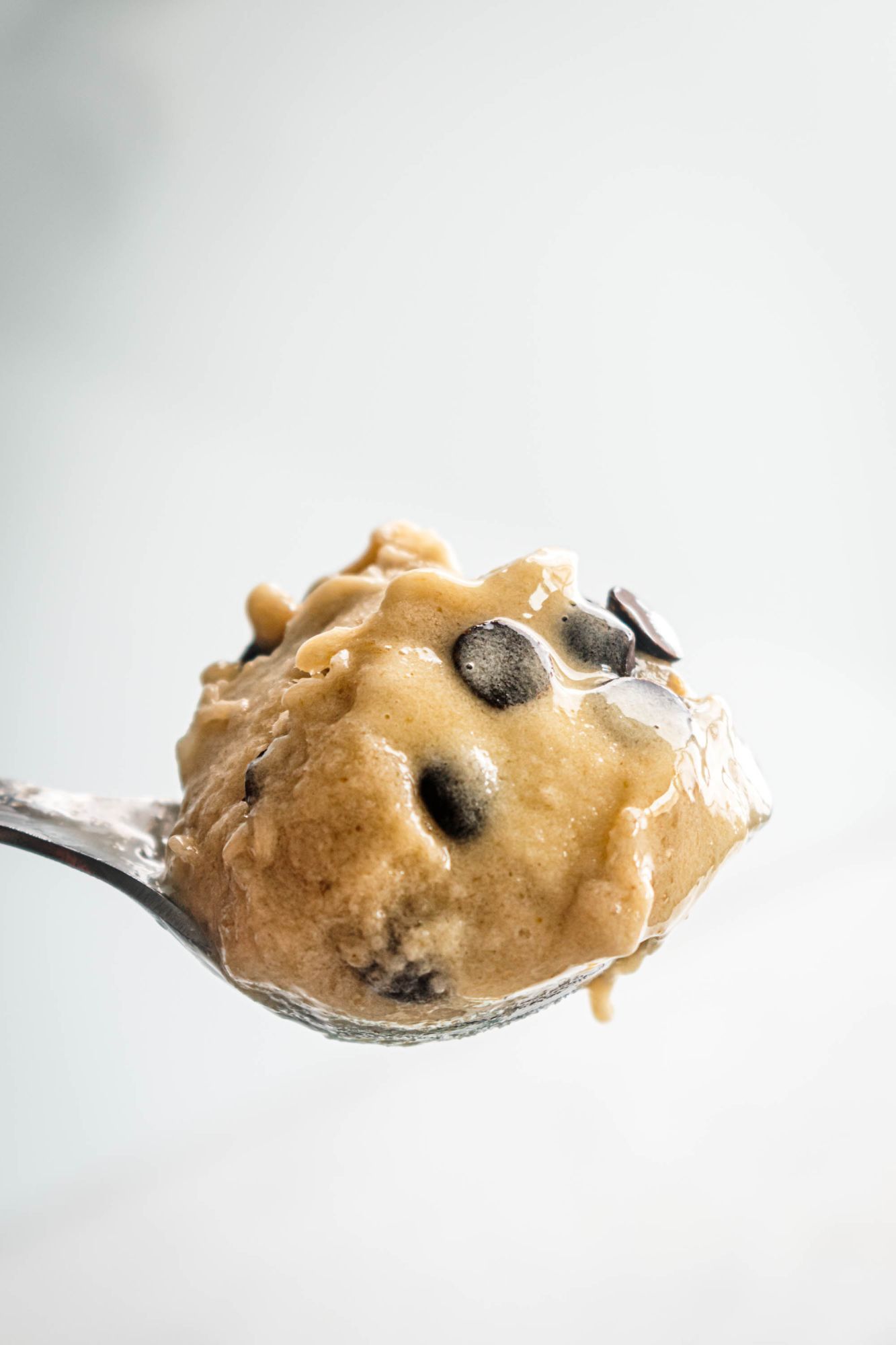 Scoop of banana ice cream with chocolate chips on metal spoon.