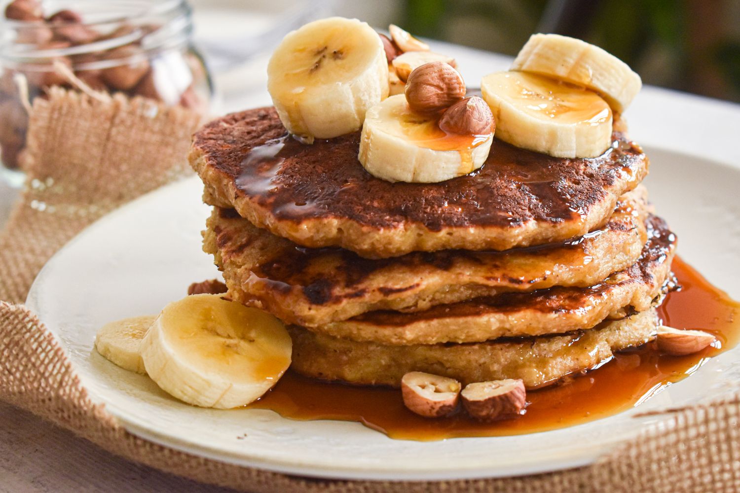 Oatmeal pancakes with bananas stacked on a plate with syrup and banana slices.