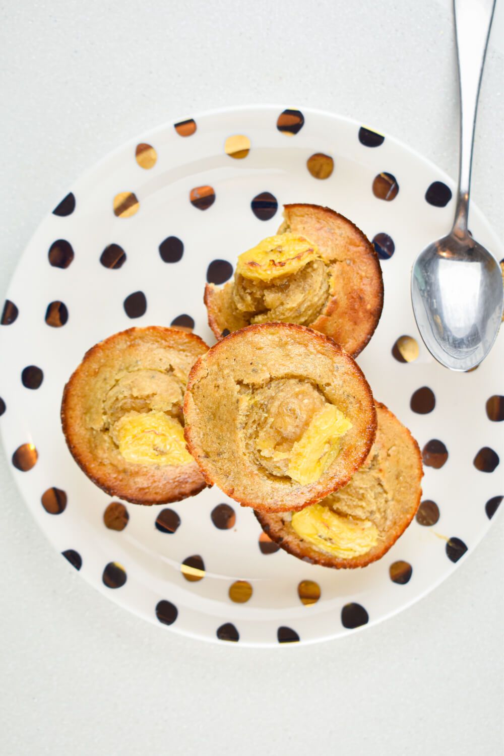 Banana quinoa muffins with chia seeds in a pile on a gold and white plate.