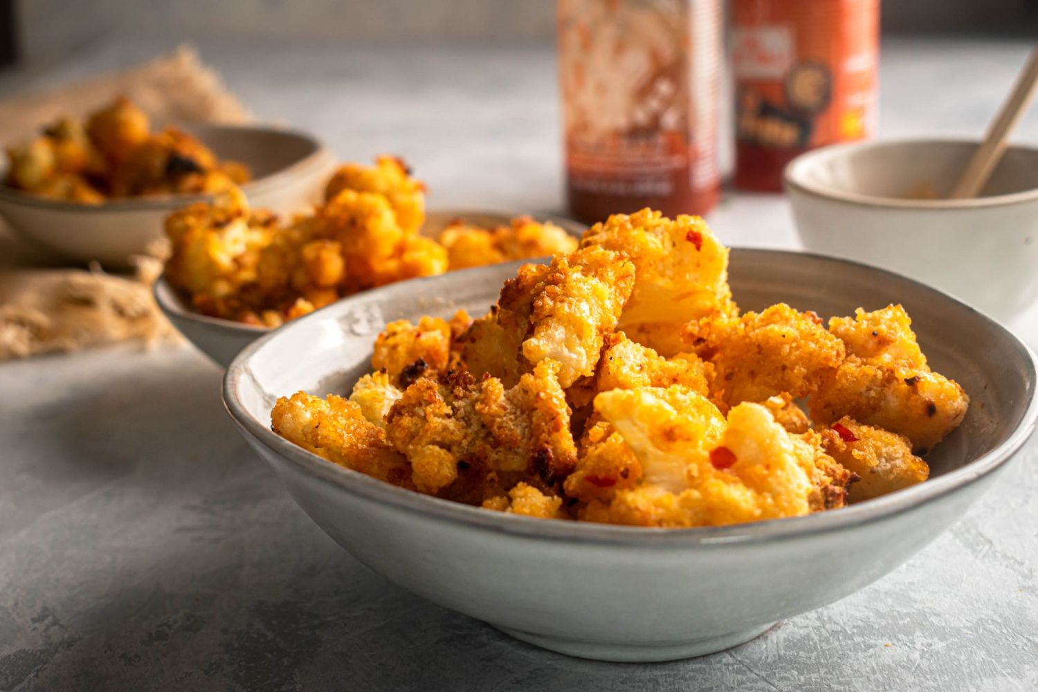 Roasted cauliflower in bang bang sauce served in two bowls with extra bang bang sauce on the side.