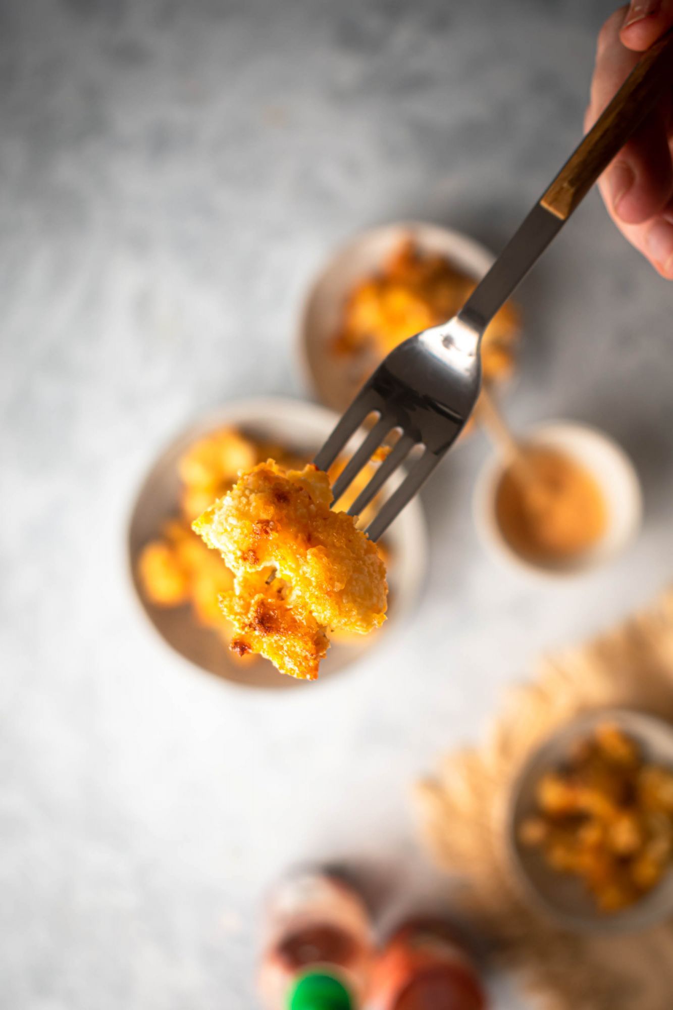 Crispy baked cauliflower with bang bang sauce on a fork with Sriracha and sweet chili sauce in the back.