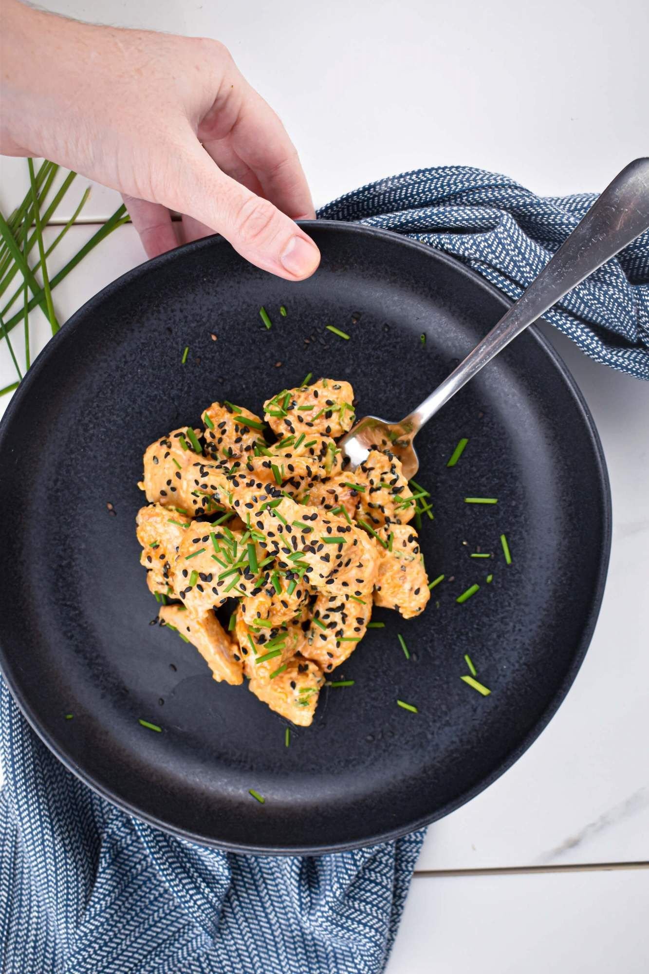 Bang Bang chicken breast on a plate with sesame seeds and green onions with a hand holding the plate.