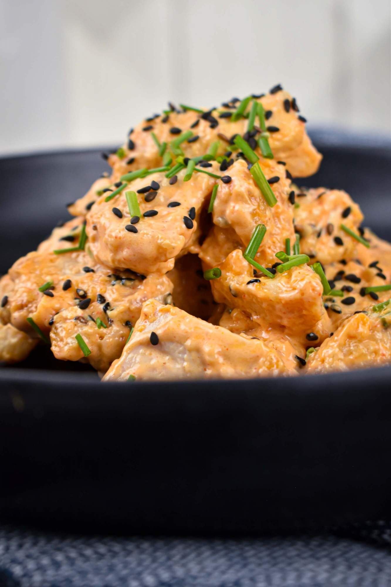 Chicken in bang bang sauce piled in a black bowl with green onions and sesame seeds.