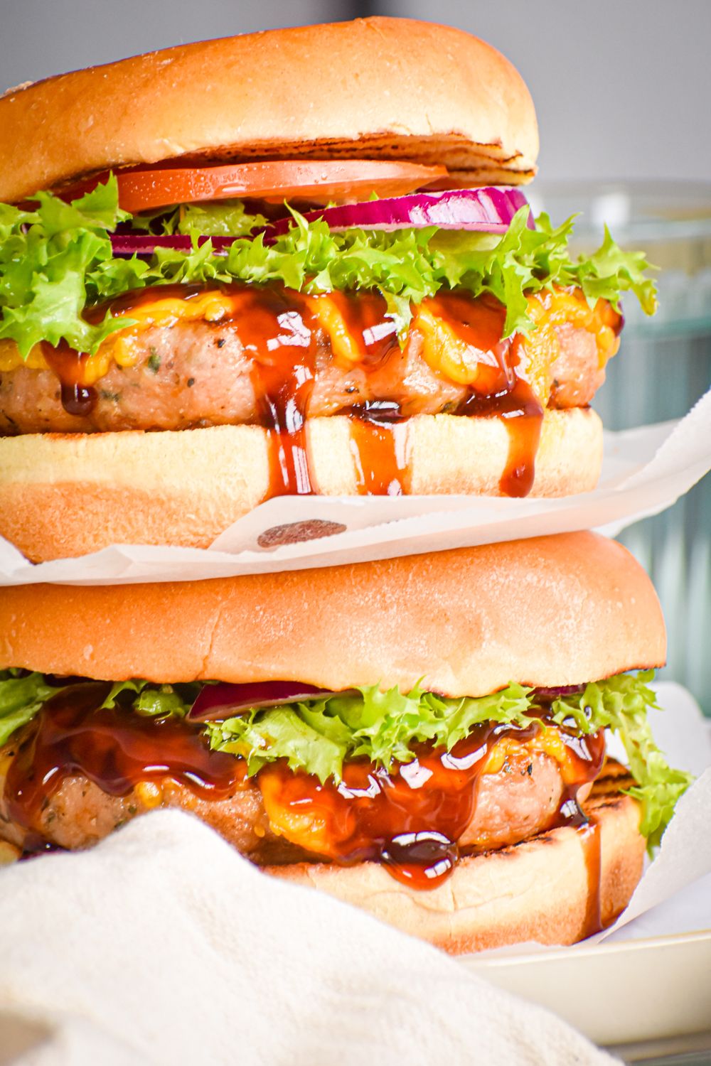 Barbecue turkey burgers with cheddar cheese placed on top of each other with lettuce, tomato, and onion.