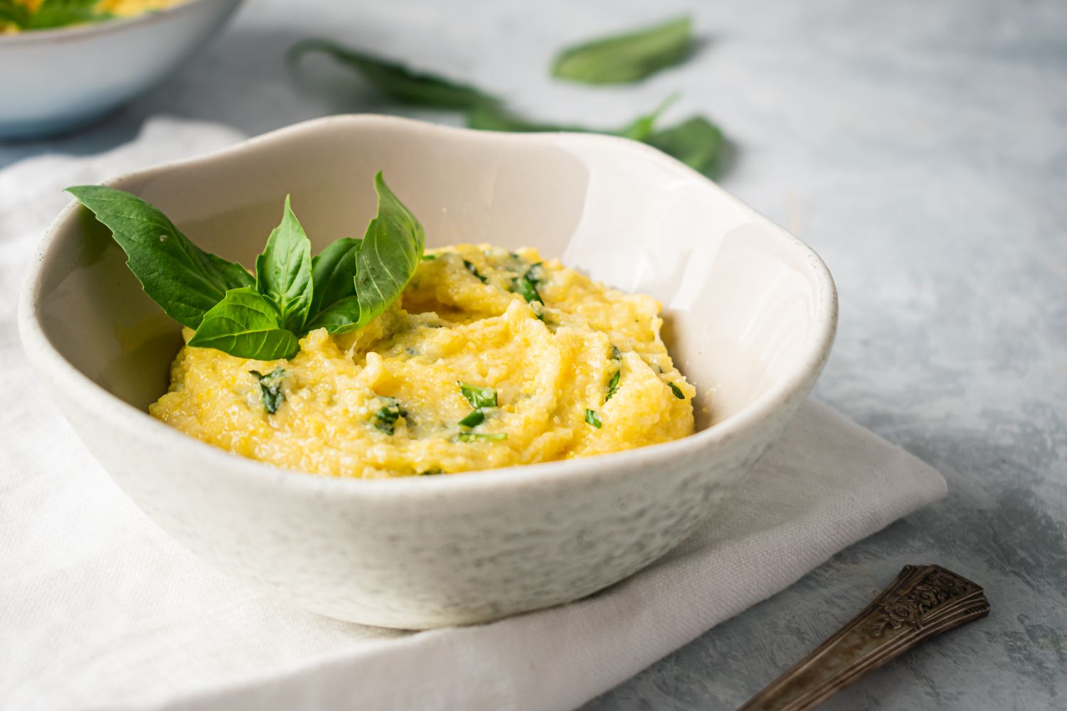 Basil Parmesan polenta in a bowl with fresh basil leaves and a white napkin.