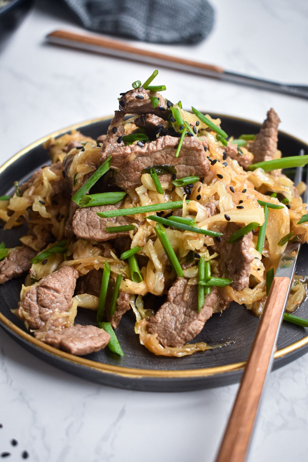 Beef stir fry with shredded cabbage, garlic, ginger, and green onions with soy sauce on a plate.