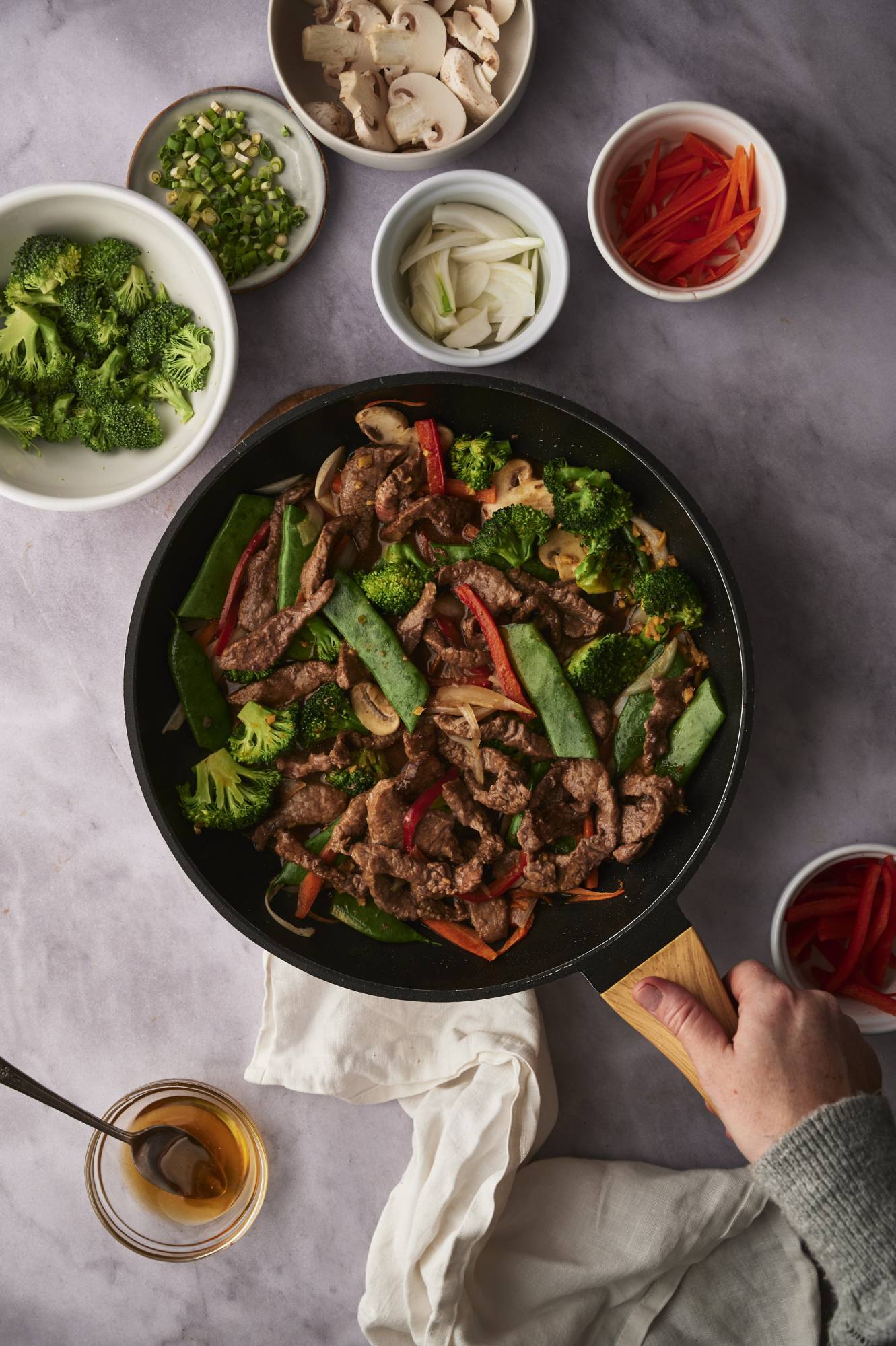 Beef and vegetable stir fry in a skillet with thinly sliced beef, broccoli, snow peas, carrots, onion, and bell pepper.