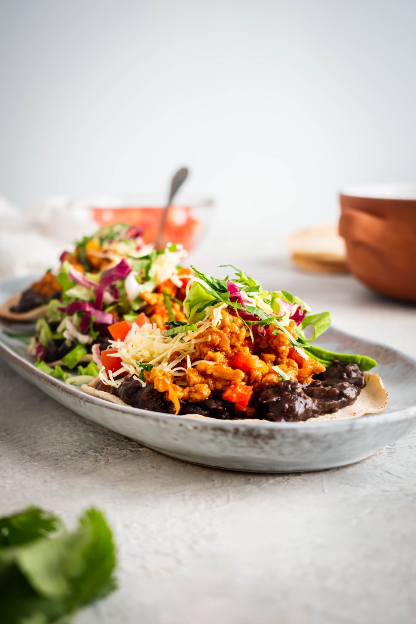 Ground beef tostadas with refried black beans, taco meat, lettuce, tomatoes, cheese, and avocado on a plate.