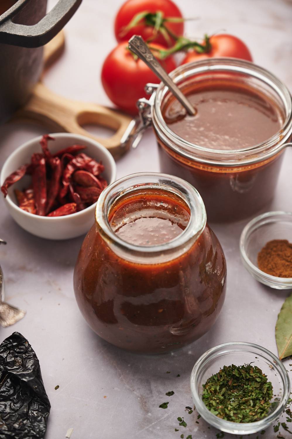 Birria consome with red dried chile sauce in two glass jars with dried peppers on the side.