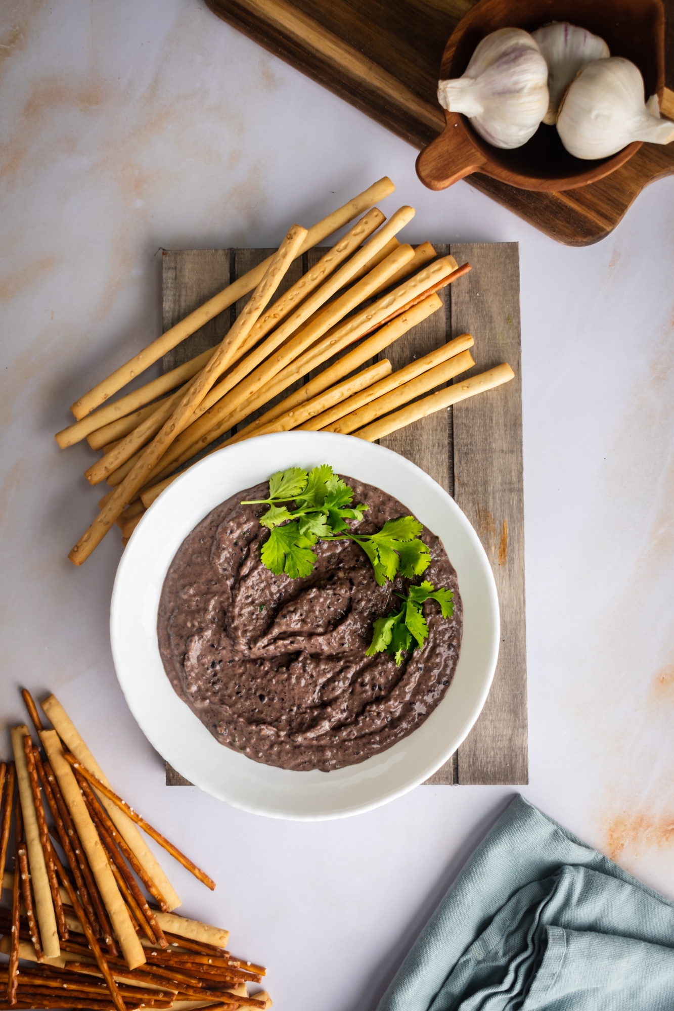 Hummus with black beans served in a bowl with cilantro and breadsticks.