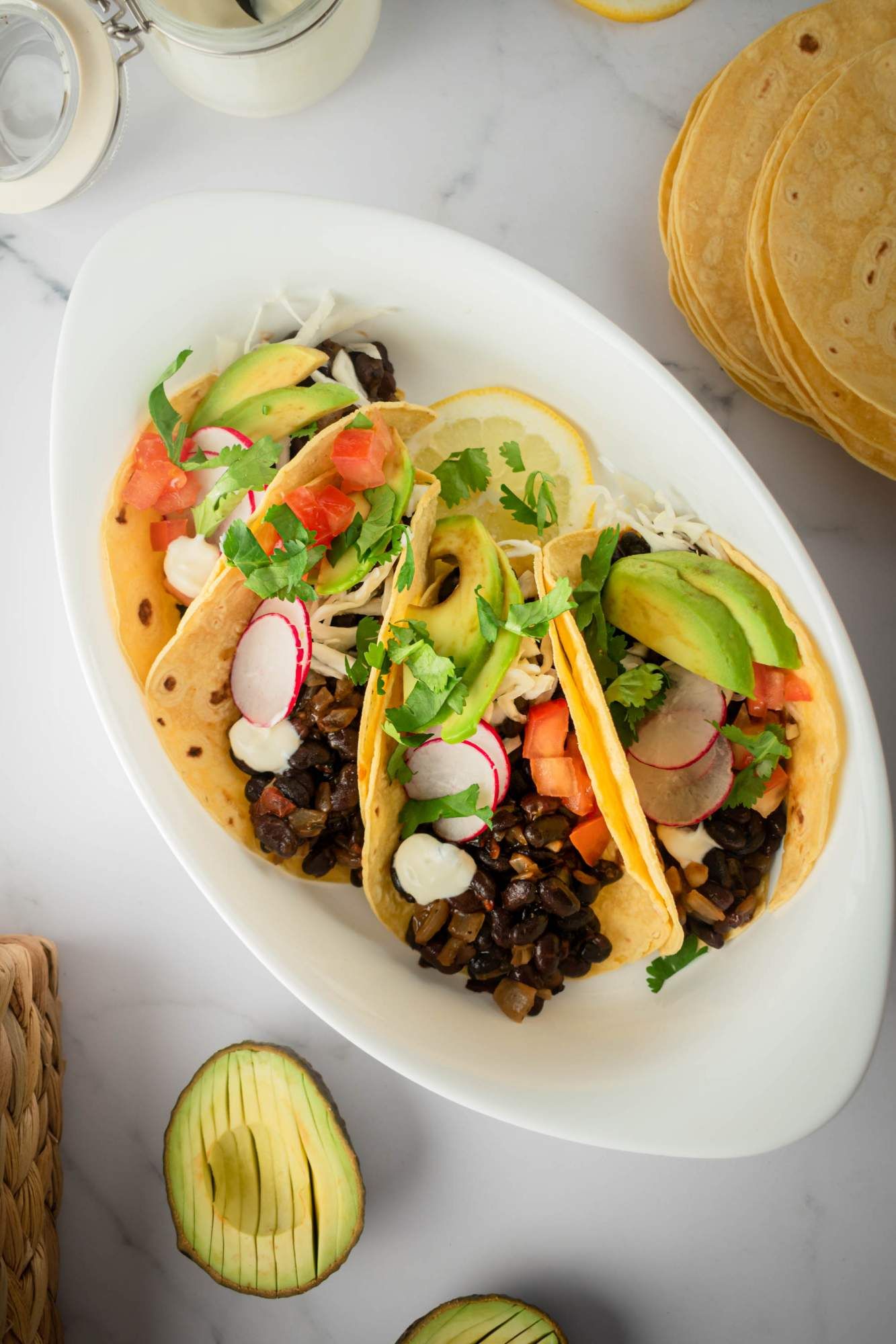 Vegetarian black bean tacos served in corn tortillas with avocado, cilantro, radishes, and tomatoes.