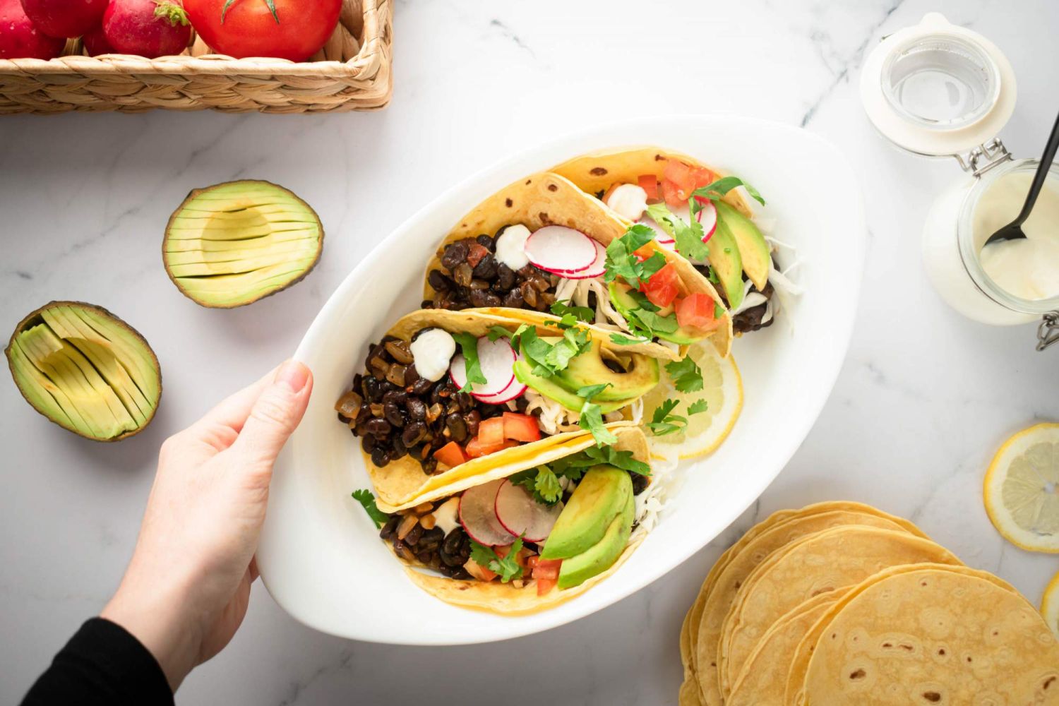 Vegan black bean tacos in corn tortillas with avocados, radishes, and tomatoes on the side.