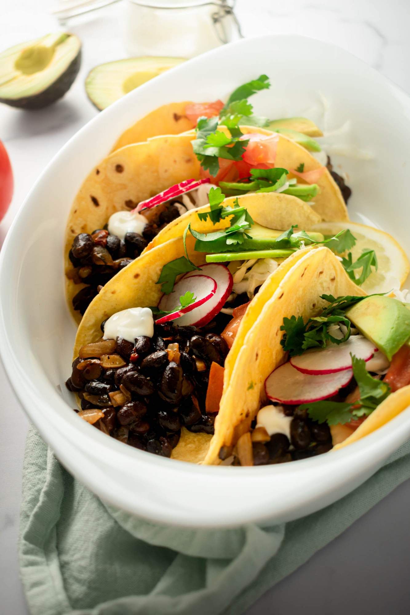 Bean tacos made with black beans, onions, tomatoes, and cilantro served in tortillas with sliced avocado.