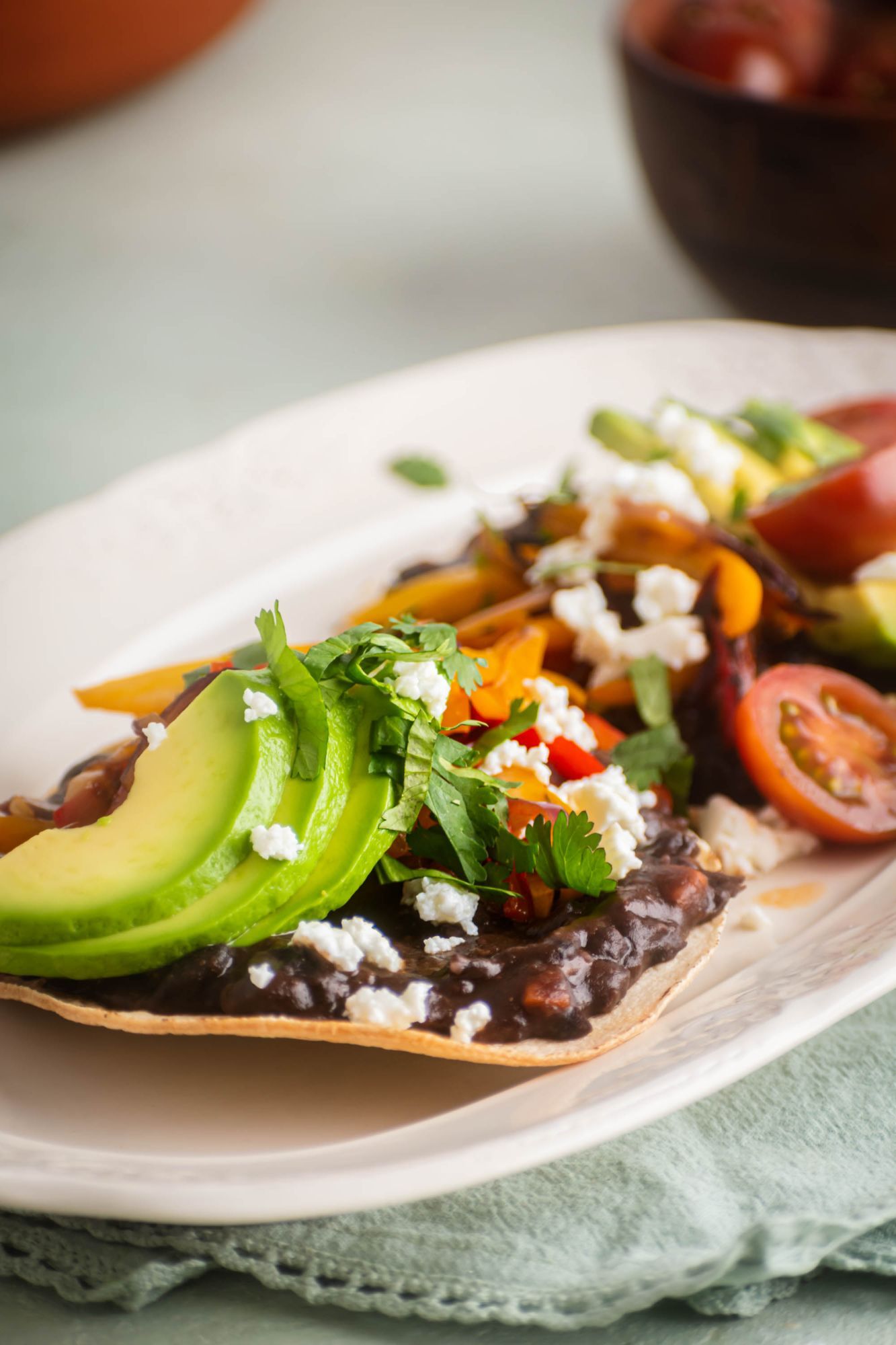 Tosadas topped with mashed beans, avocado, queso fresco, tomatoes, peppers, and onions.