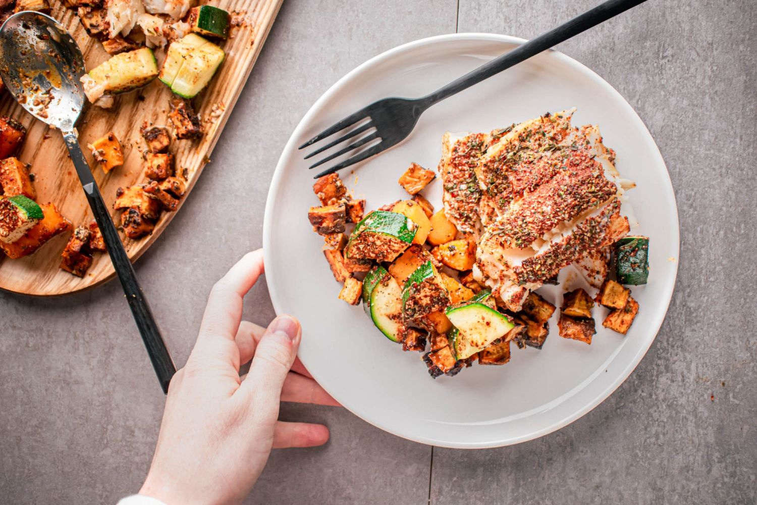 Cod with blackening seasoning served on a plate with roasted sweet potatoes and zucchini.