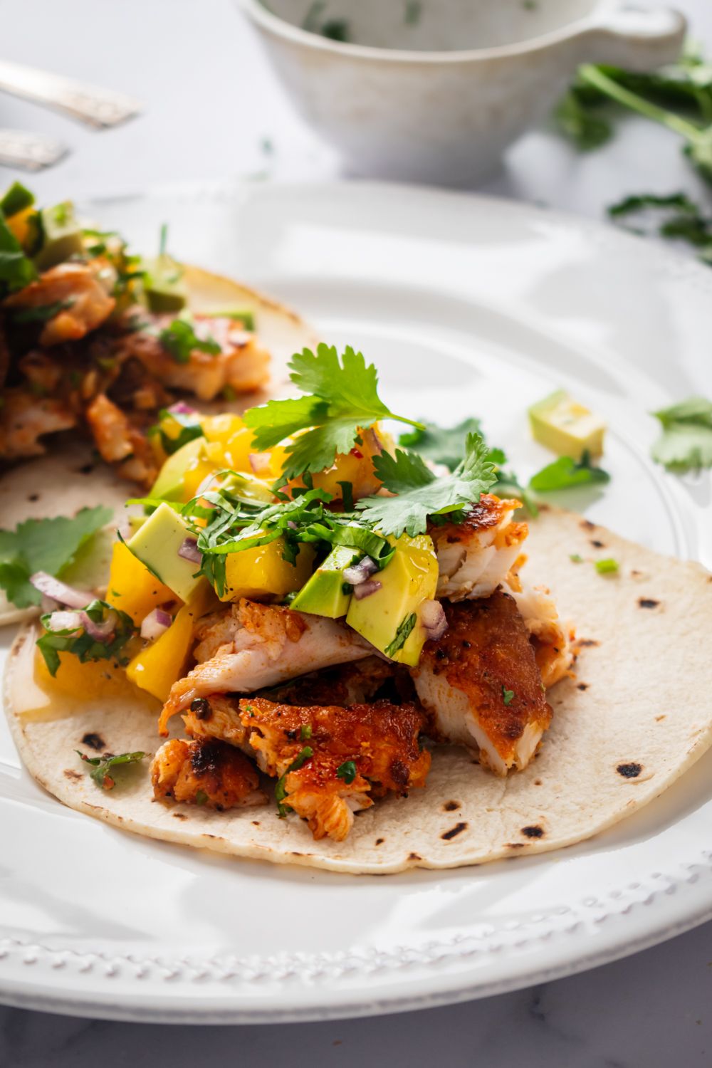 Fish tacos with blackening seasoning and served with mango salsa on corn tortillas.