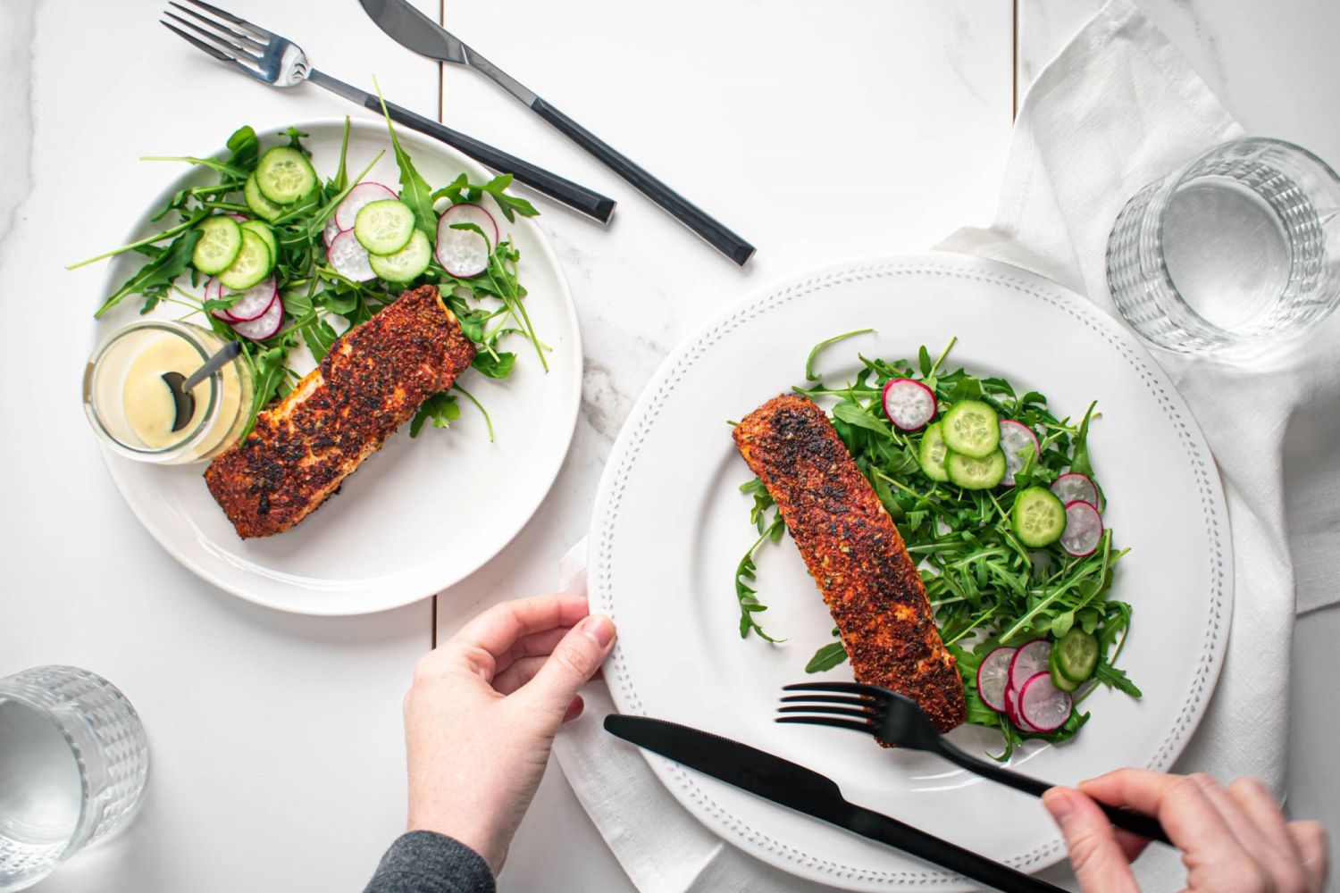 Crispy blackened salmon with a dark spice coating on two plates with salad greens.