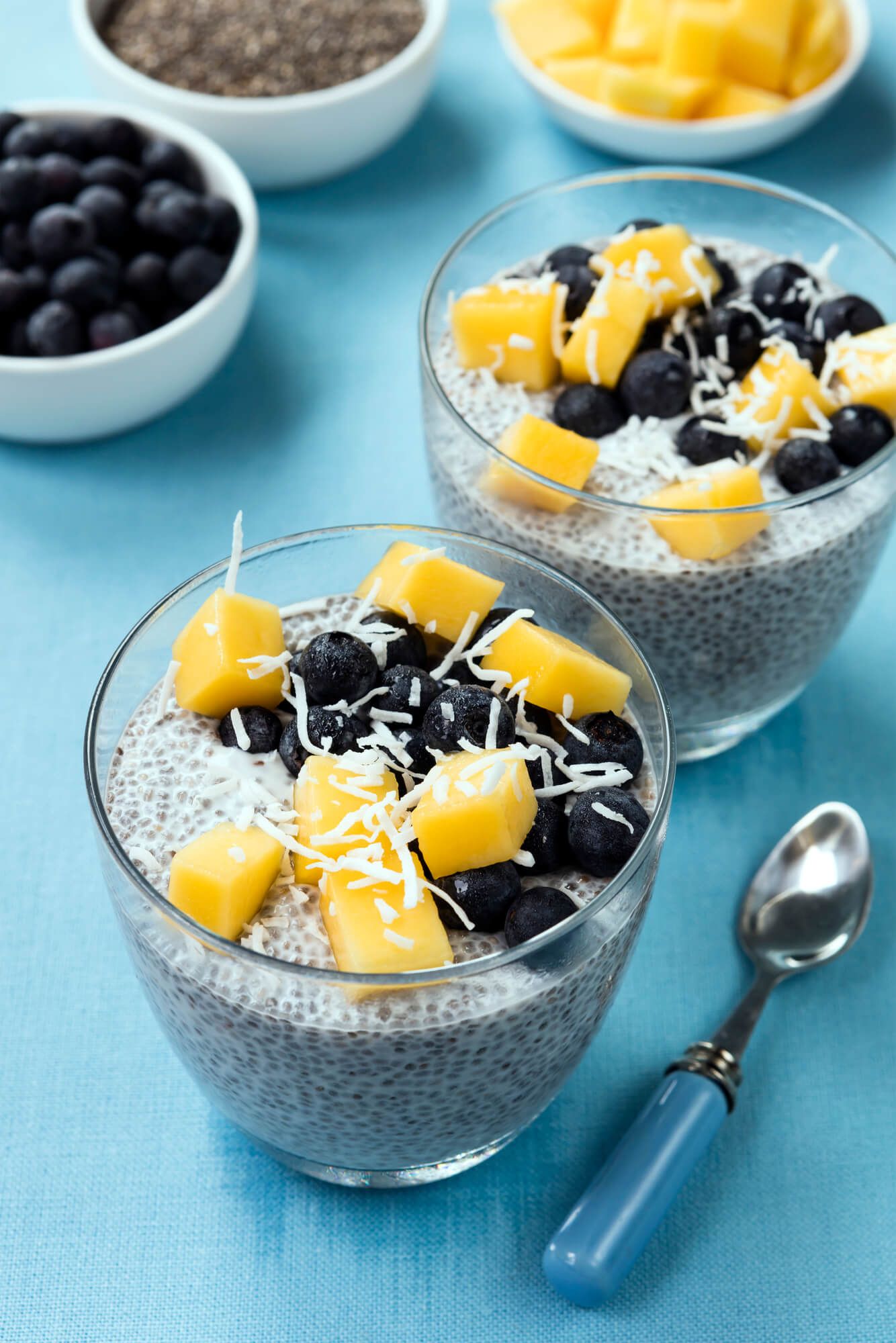 Two cups with blueberry coconut chia seed pudding topped with mango, blueberries, and coconut.