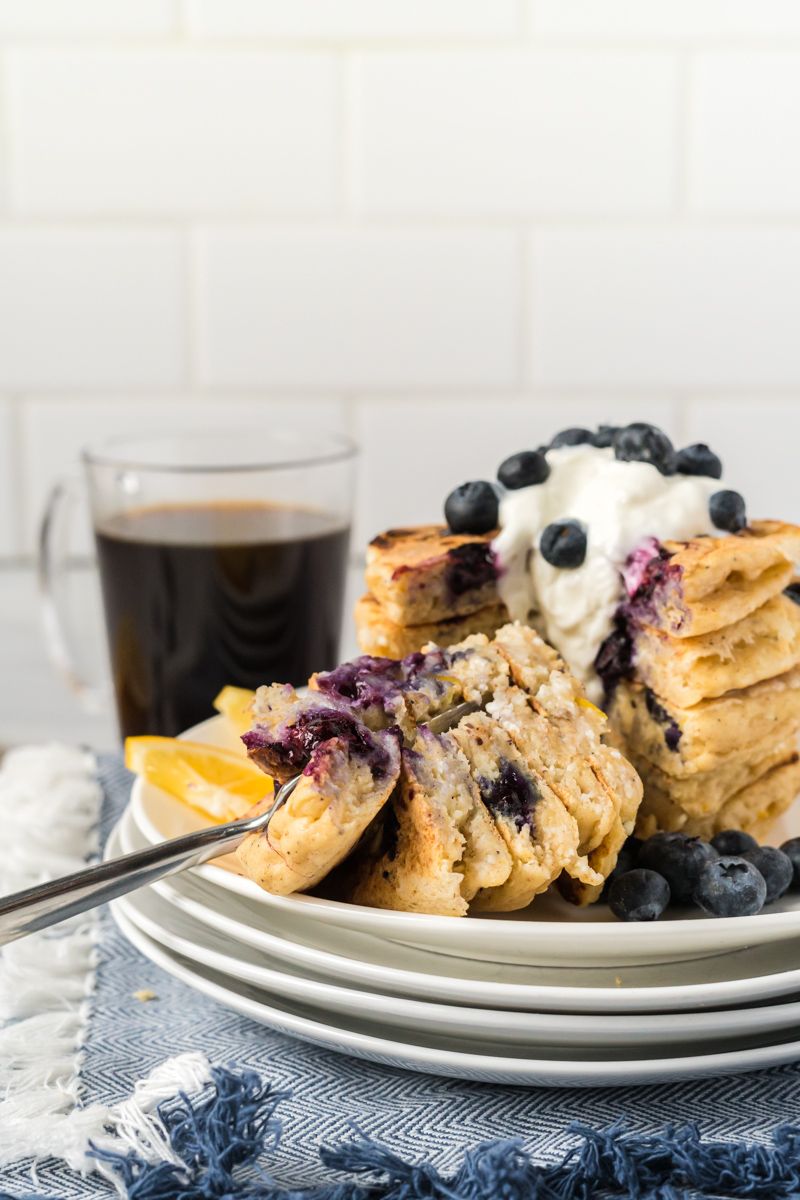 Blueberry ricotta pancakes with fresh lemon juice in a stack with a fork taking a bite.