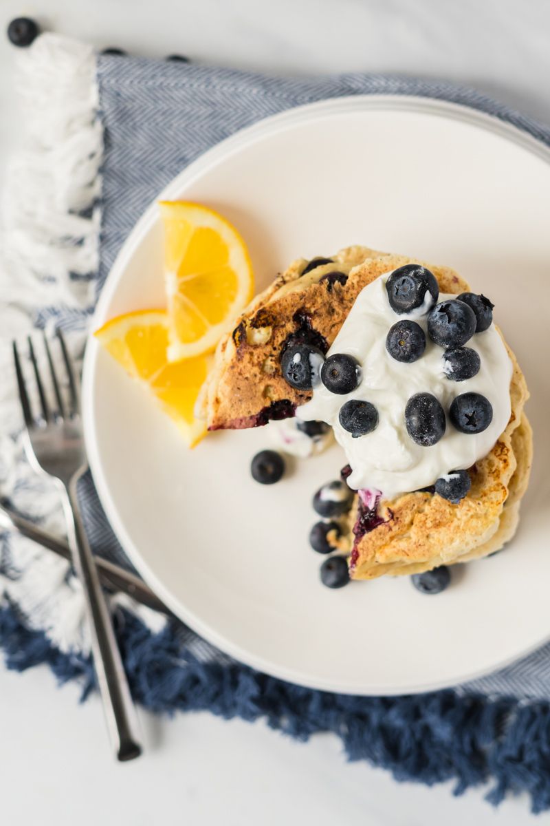 Ricotta pancakes with blueberries and lemon on a plate with Greek yogurt and blueberries on top.