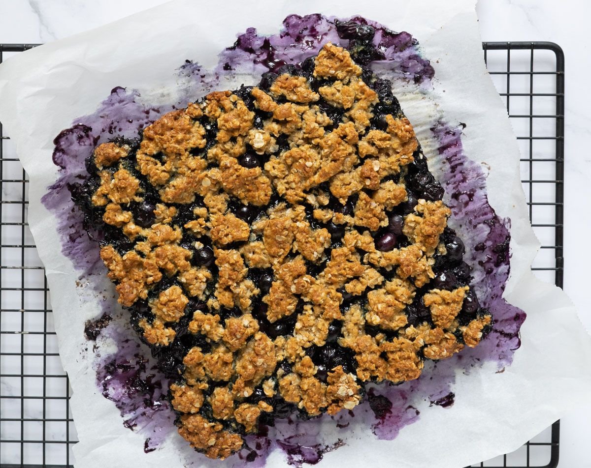 Blueberry oatmeal bars with whole blueberries and a crumbly topping on a piece of parchment paper