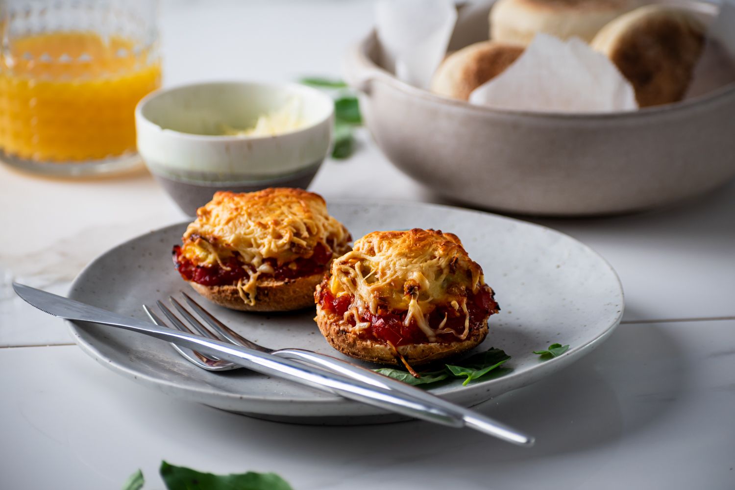 Breakfast pizzas with English muffins topped with scrambled eggs, sauce, and cheese with orange juice on the side,