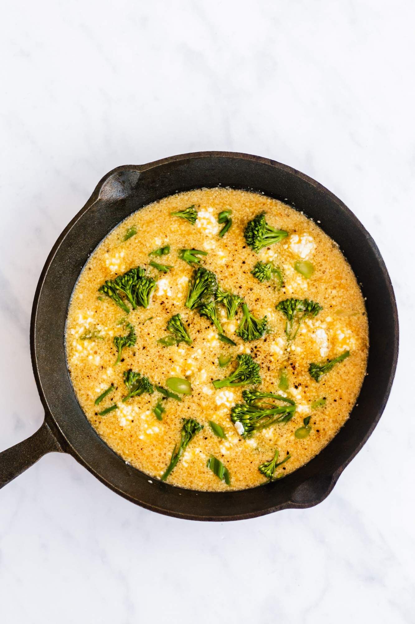 Frittata with broccoli, eggs, and cheese in a cast iron skillet before being cooked.