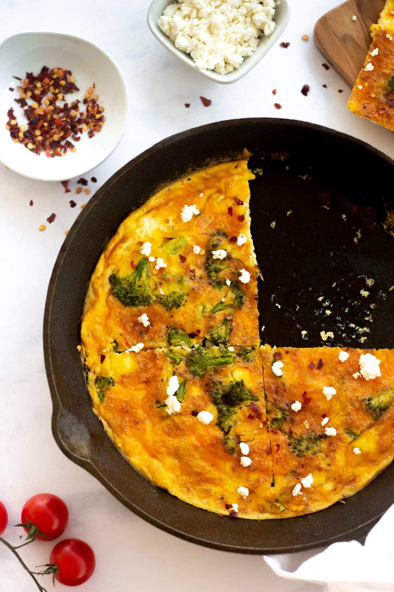 Cheese and broccoli frittata cooked in a cast iron skillet with one sliced cut out.