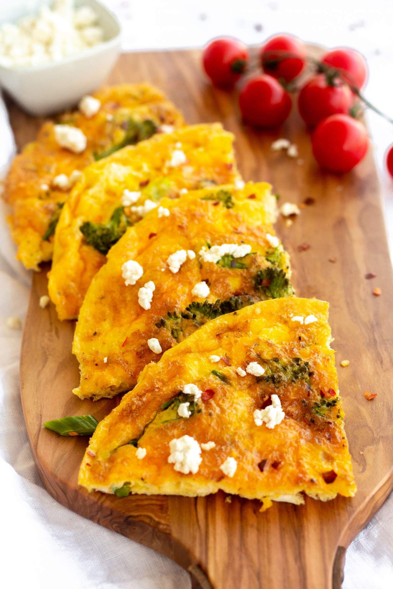 Broccoli frittata with cheese cut into slices and served on a cutting board with tomatoes.