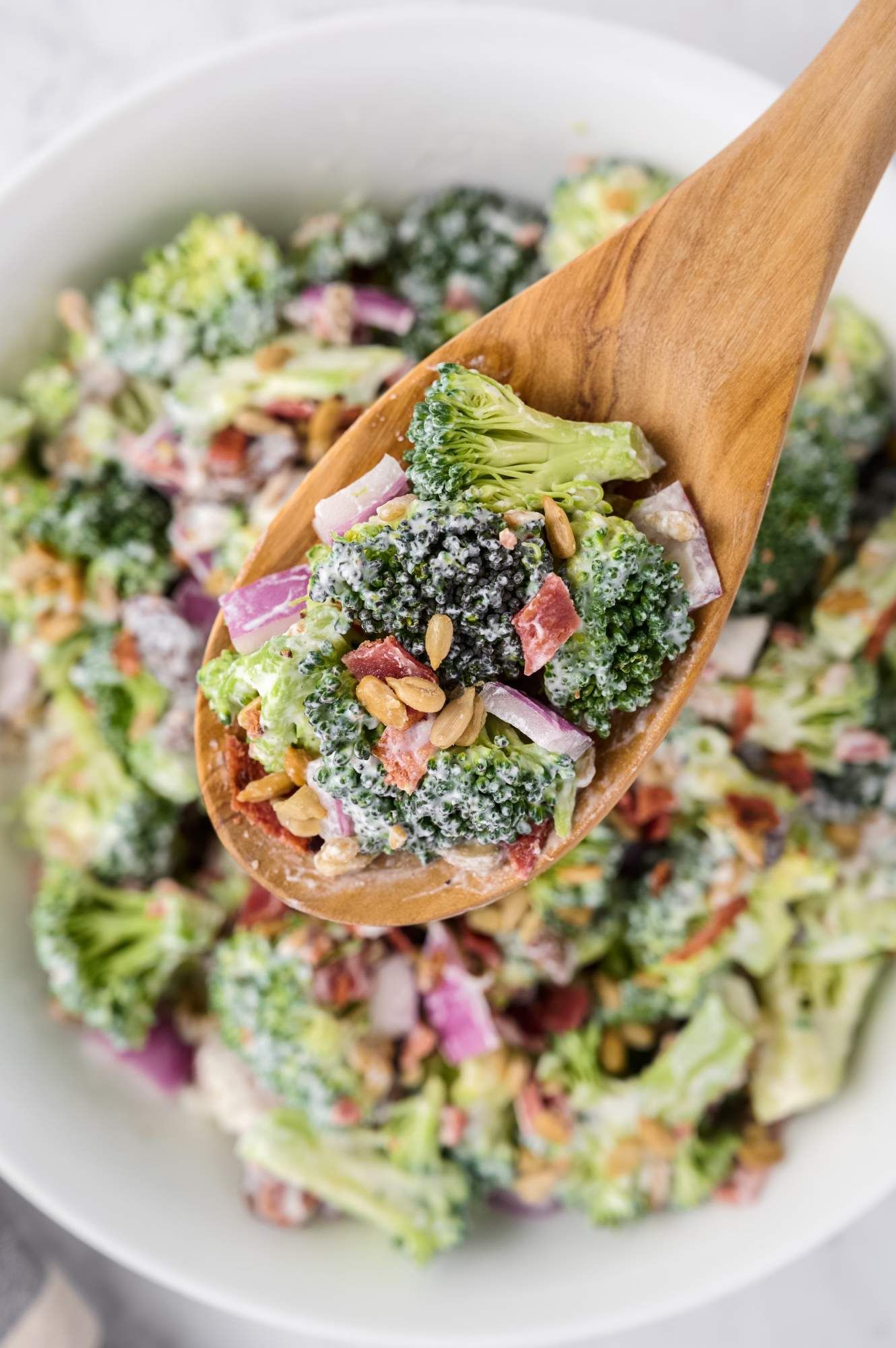 Creamy broccoli salad on a wooden spoon with fresh broccoli, turkey bacon, and raisins in a yogurt dressing.