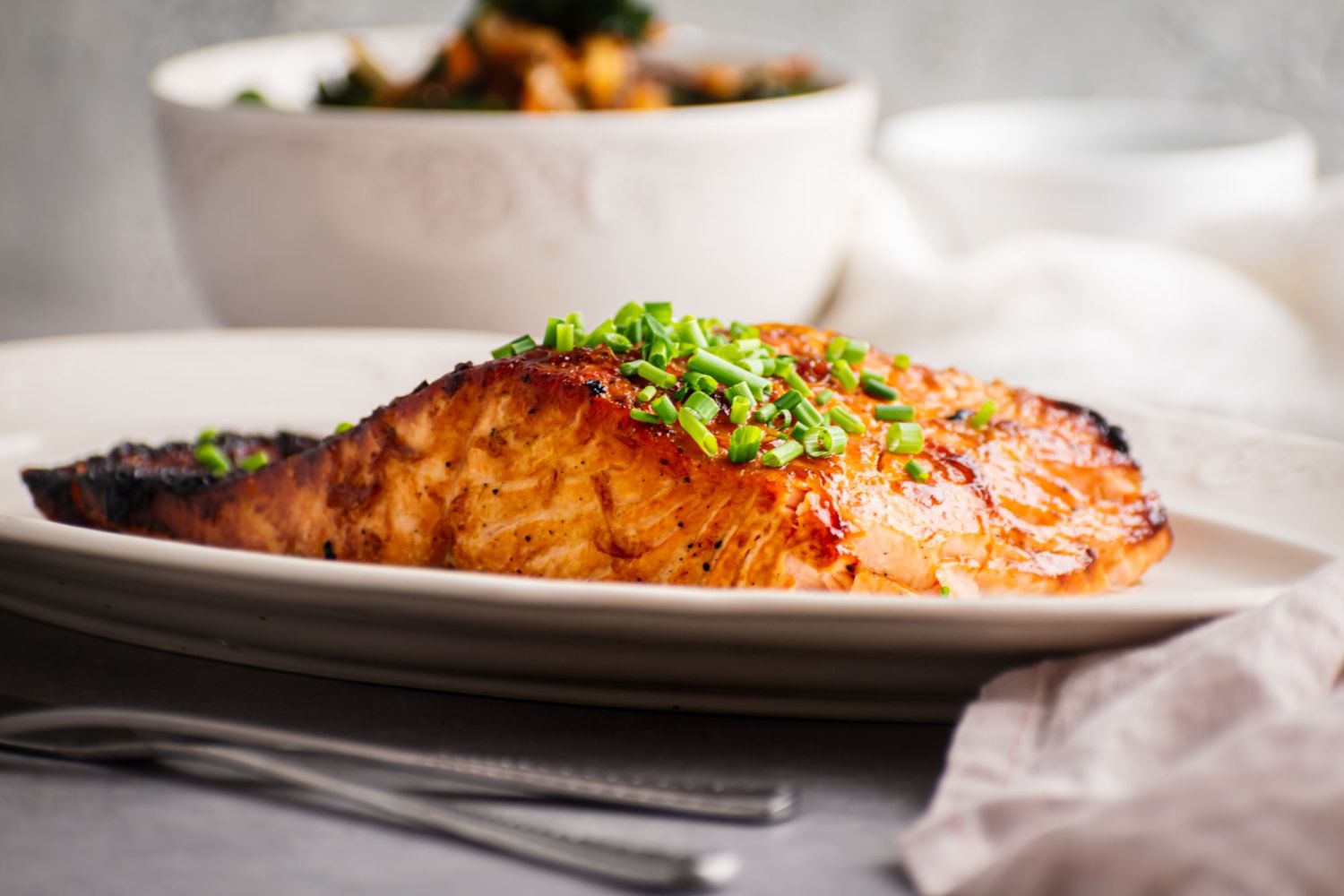 Crispy brown sugar glazed salmon served on a white plate with stir fried vegetables on the side.