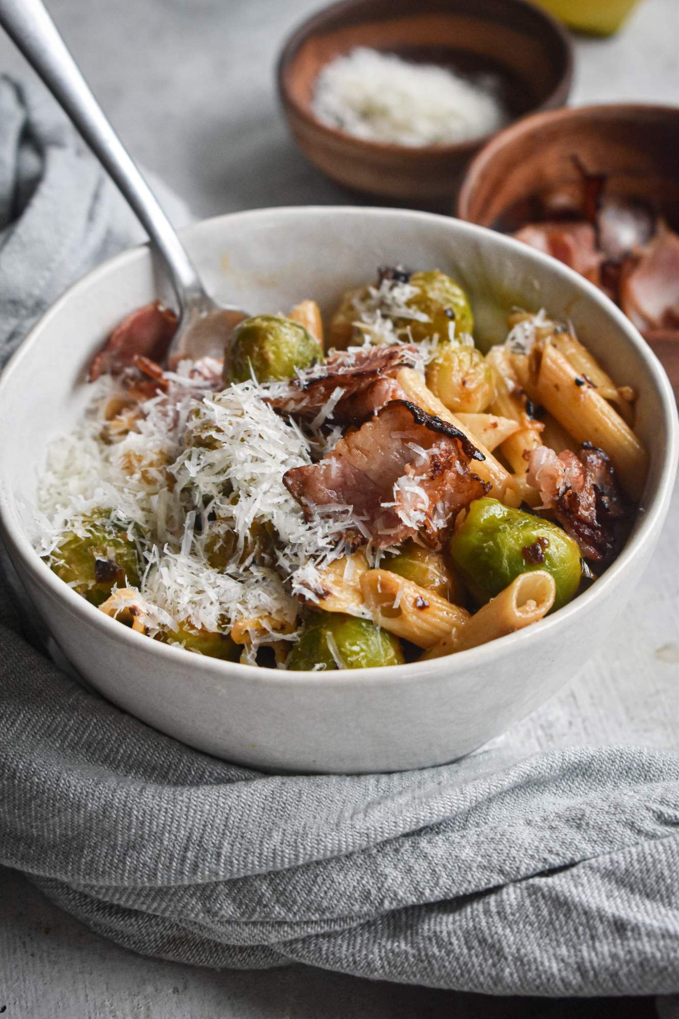 Brussels sprouts and bacon pasta with fresh lemon juice and Parmesan cheese in a bowl with a spoon. 