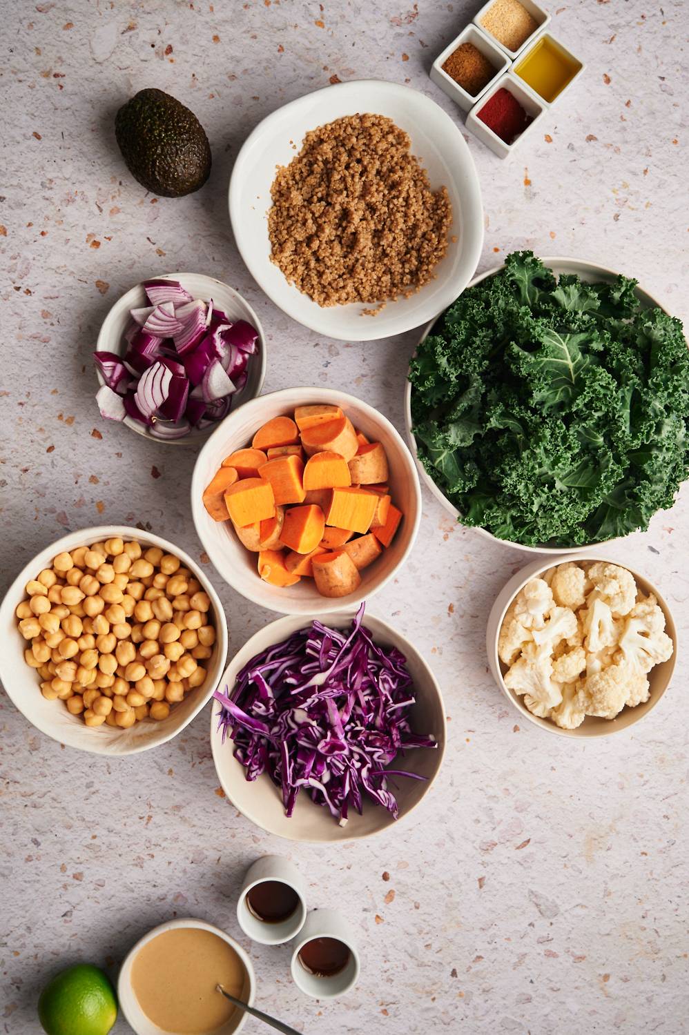 Ingredients for a buddha bowl including kale, quinoa, sweet potatoes, cauliflower, purple cabbage, and onions.