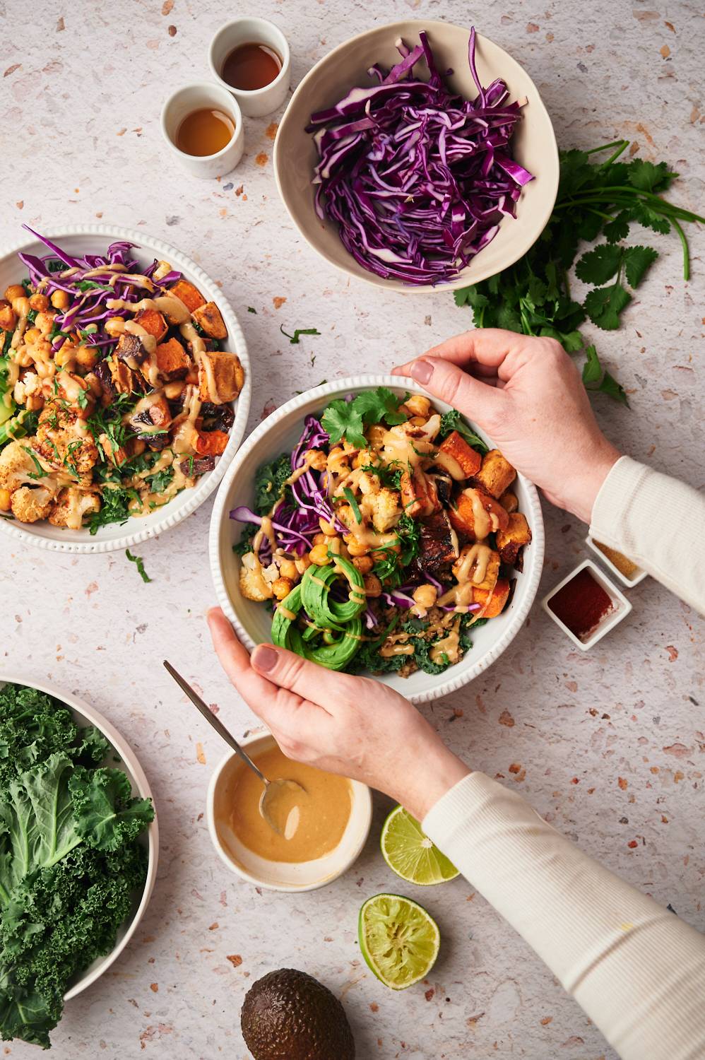 Vegan buddha bowl with quinoa, kale, chickpeas, cauliflower, sweet potatoes, and tahini dressing in a bowl being held by two hands.