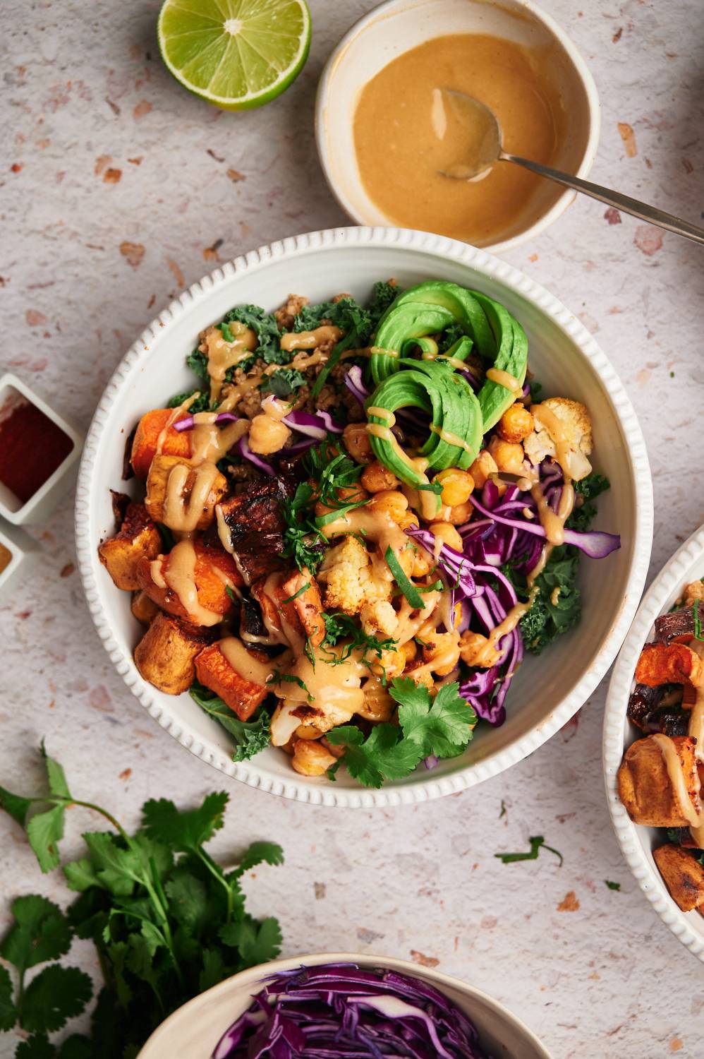 Grain bowl with quinoa, kale, avocado, sweet potatoes, onions, cauliflower, and chickpeas served with tahini dressing and herbs.