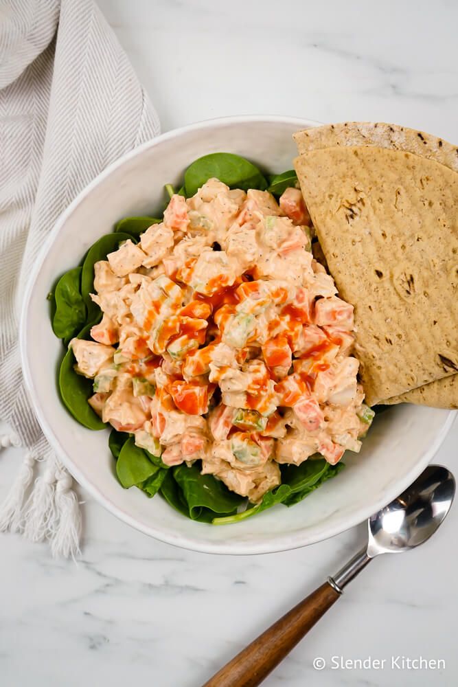 Chicken salad with buffalo sauce on a bed of spinach with a whole wheat wrap.