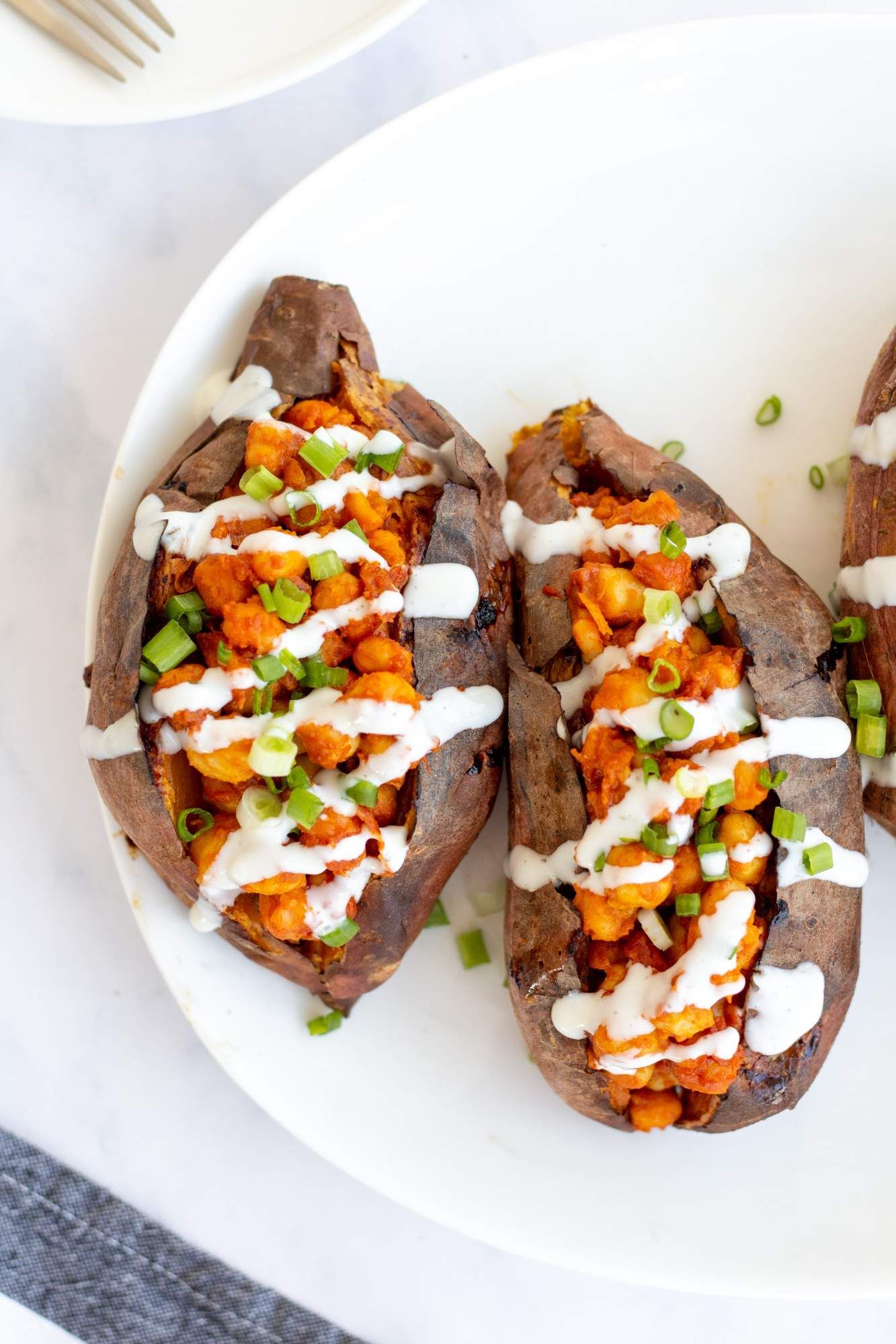 Buffalo sweet potatoes with chickpeas drizzled with ranch dressing and green onins on a plate.