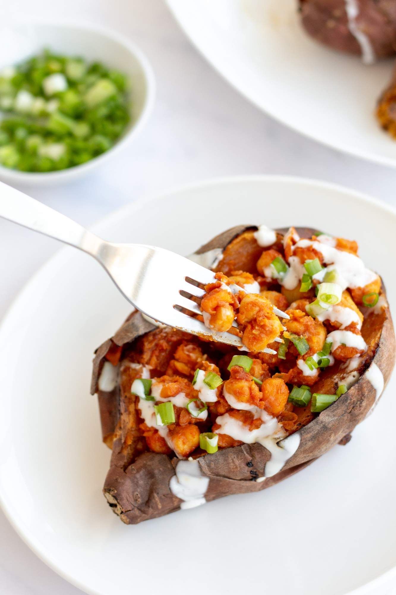 Stuffed sweet potato with buffalo chickpeas on a plate with a fork.