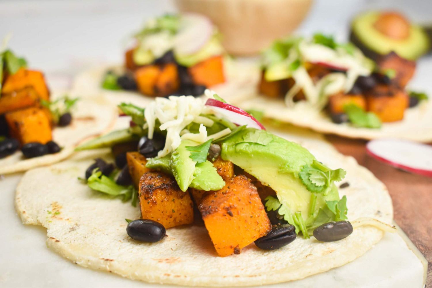 Butternut squash and black bean tacos with avocado, radish, cilantro, and onion on a corn tortilla.