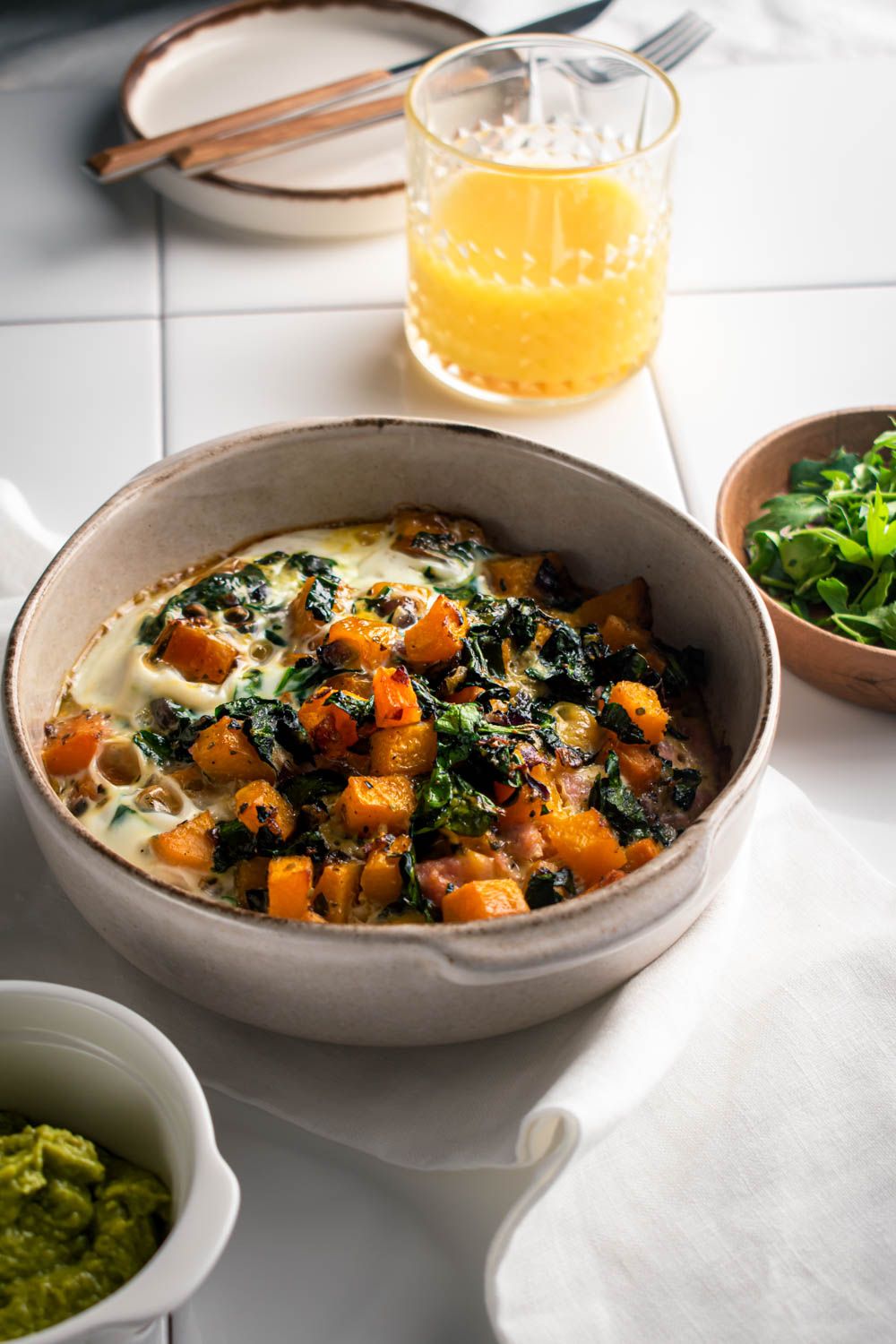 Egg casserole with butternut squash and spinach in a dish with a fork and knife on the side.