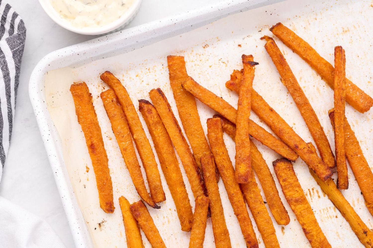 Baked butternut squash french fries on a baking sheet with dipping sauces.