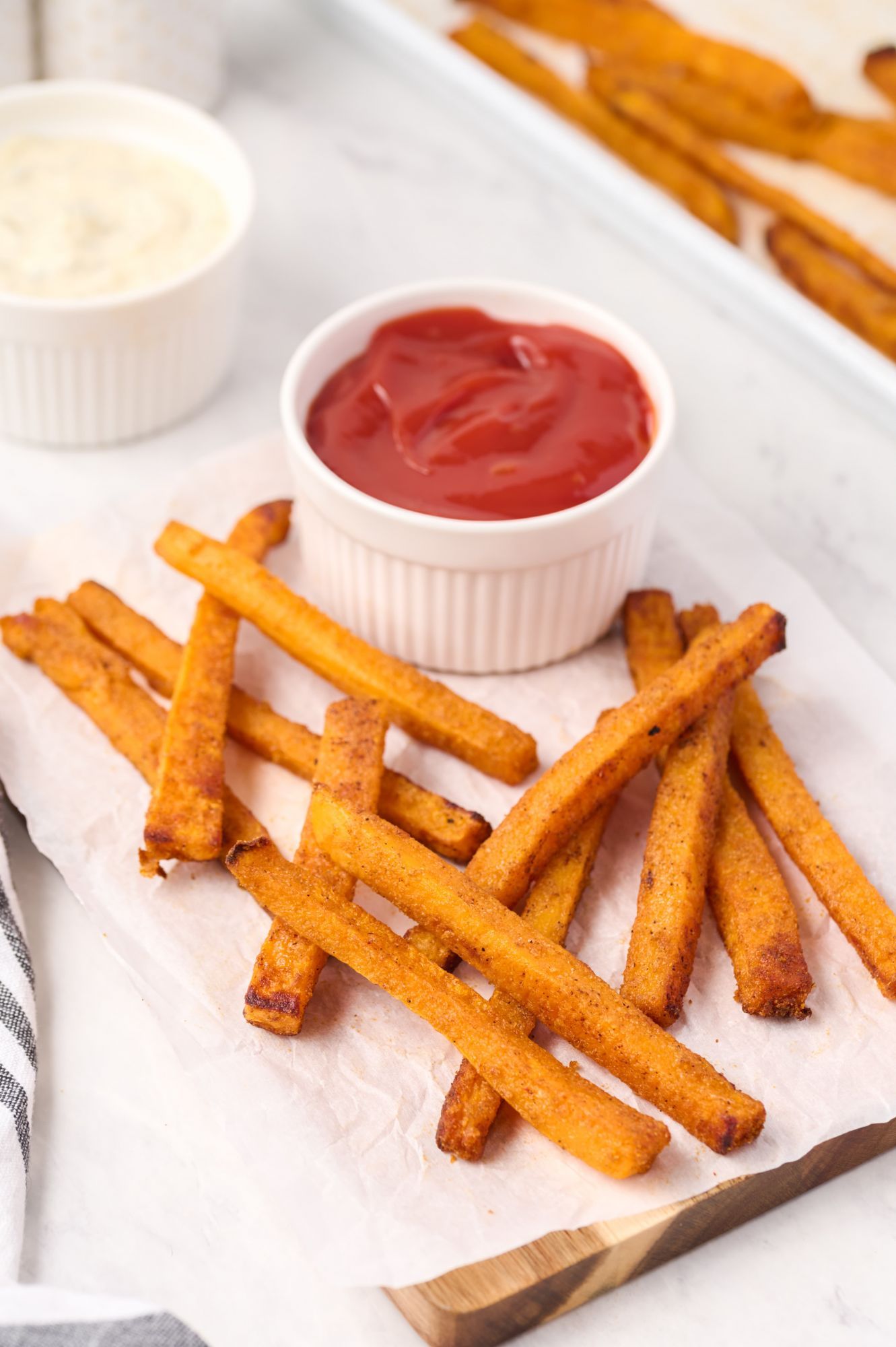 Oven baked squash fries baked until golden brown and served with ketchup on a cutting board.