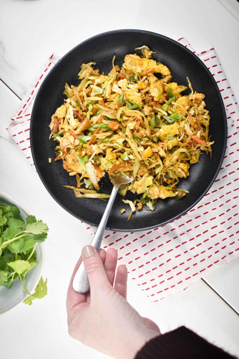 Cabbage fried rice with eggs, carrots, scallions, garlic, and ginger on a plate with cilantro.