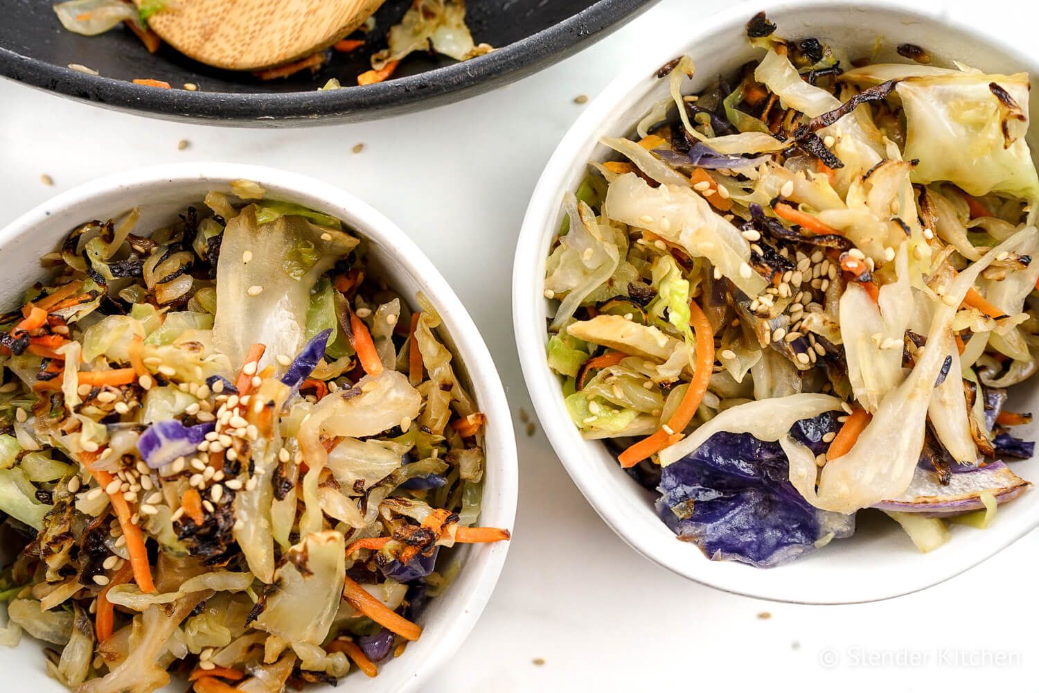 Cabbage stiry fry in two white bowls topped with sesame seeds.