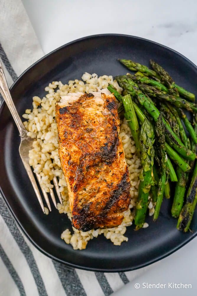 Cajun Salmon with brown rice and grilled asparagus on a black plate.