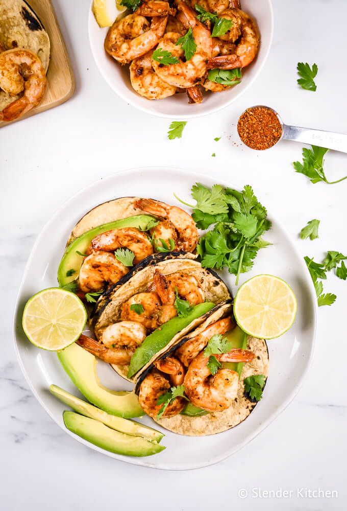 Shrimp tacos with Cajun seasoning with corn tortillas, avocado, limes, and cilantro.