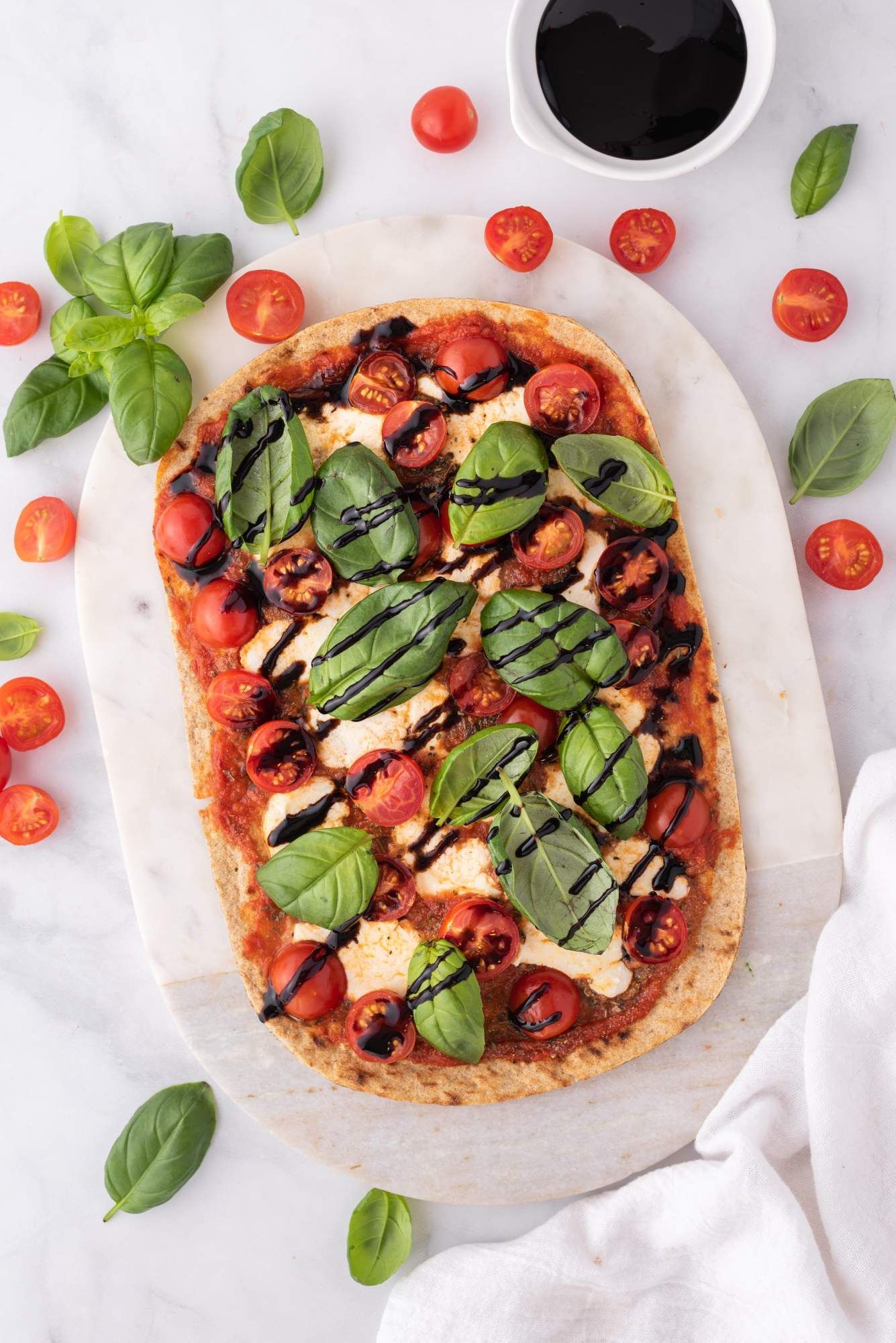 Flatbread with caprese flavors including fresh tomatoes, mozzarella, sauce, and basil leaves on a flatbead.