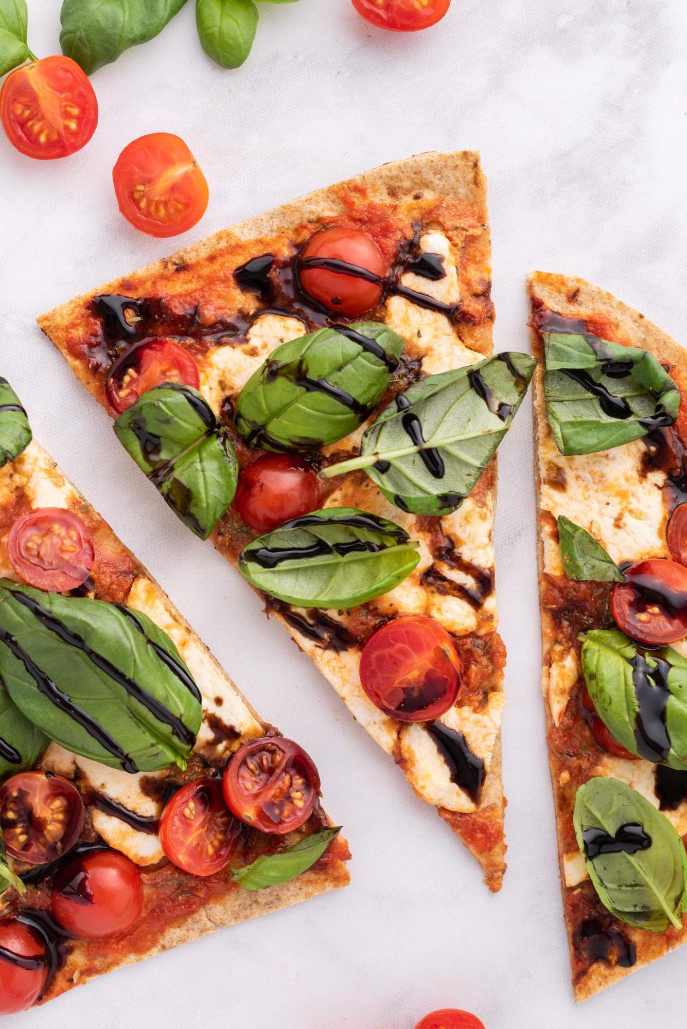 Caprese pizza flatbread on a low carb wrap with sauce, cherry tomatoes, melted cheese, basil, and balsamic glaze.