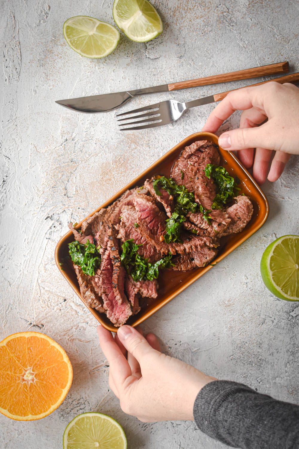 Marinated carne asada made with flank steak marinated in lime juice sliced on a plate with fresh cilantro.